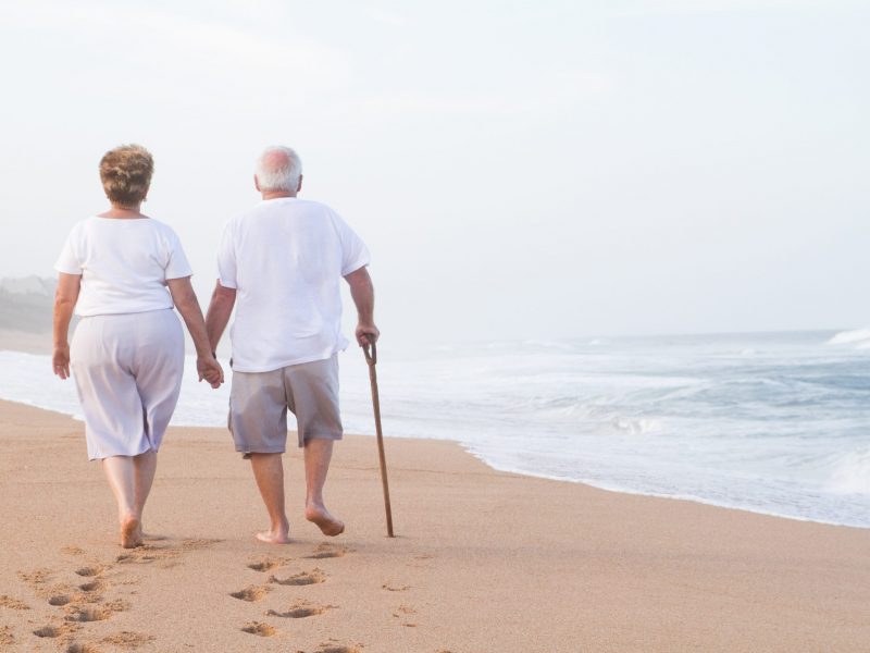 senior couple hand in hand walking on beach